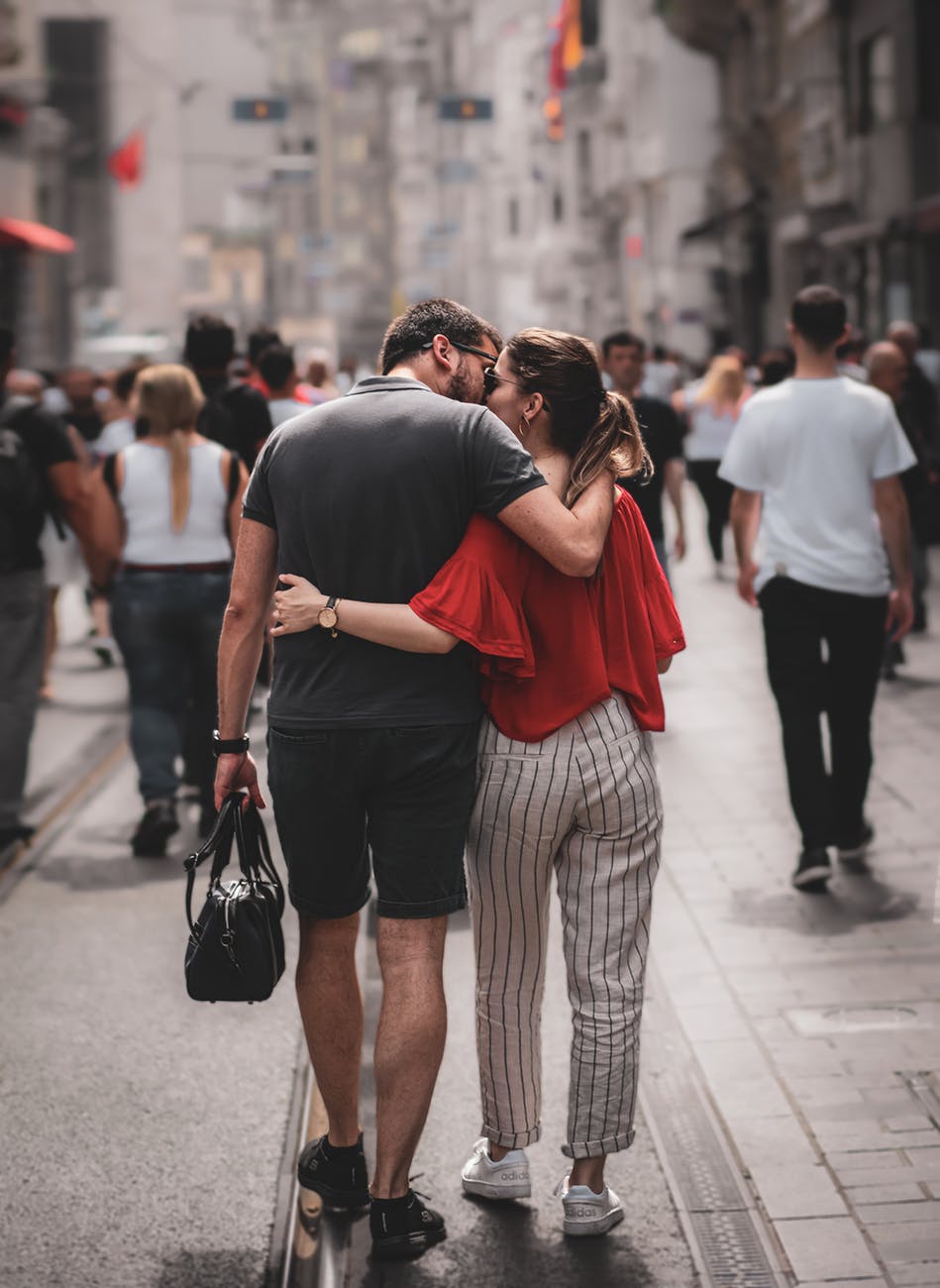 man kissing woman while walking on streets